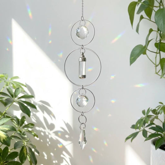 Crystal wind chime with glass spheres and a teardrop shape hanging against a light background with plant shadows.