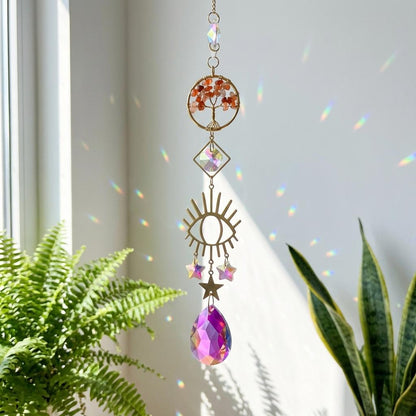 Decorative hanging crystal with sun and eye design in front of a window with plants.