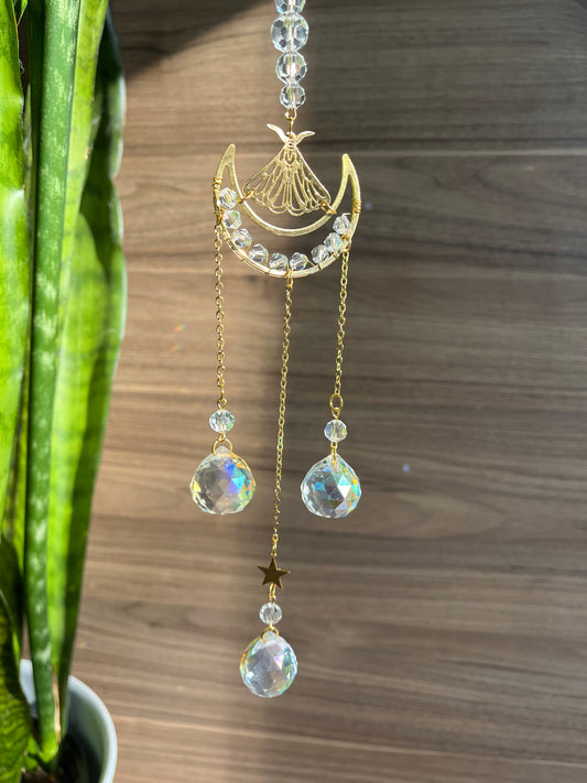 A gold-colored wind chime with a moth design and three dangling crystals placed above a wooden surface.
