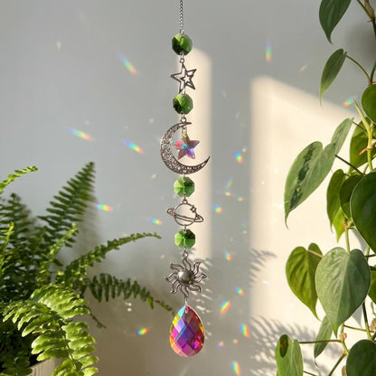 Decorative hanging ornament with celestial elements and a rainbow prism in front of green plants.