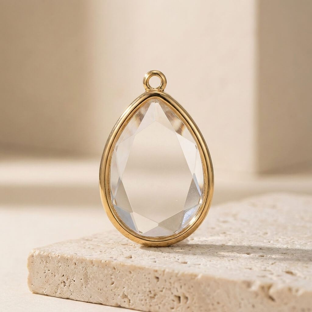 Teardrop-shaped crystal pendant with gold frame on a beige stone surface